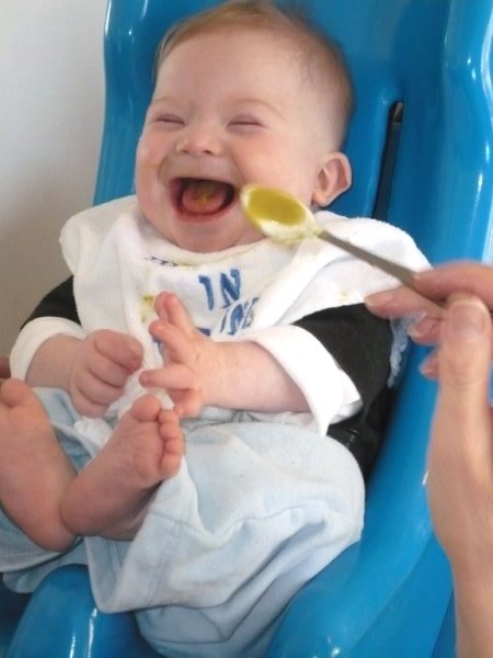 Raphael laughing in Tumbleform with baby spoon of green puree.