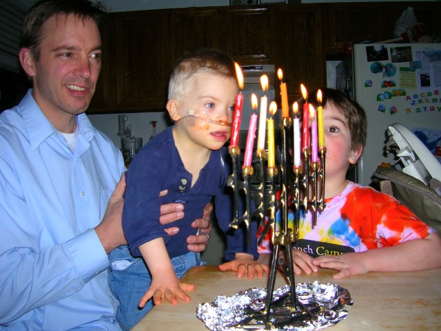 Father showing his sons the fully lit Hanukkah menorah.
